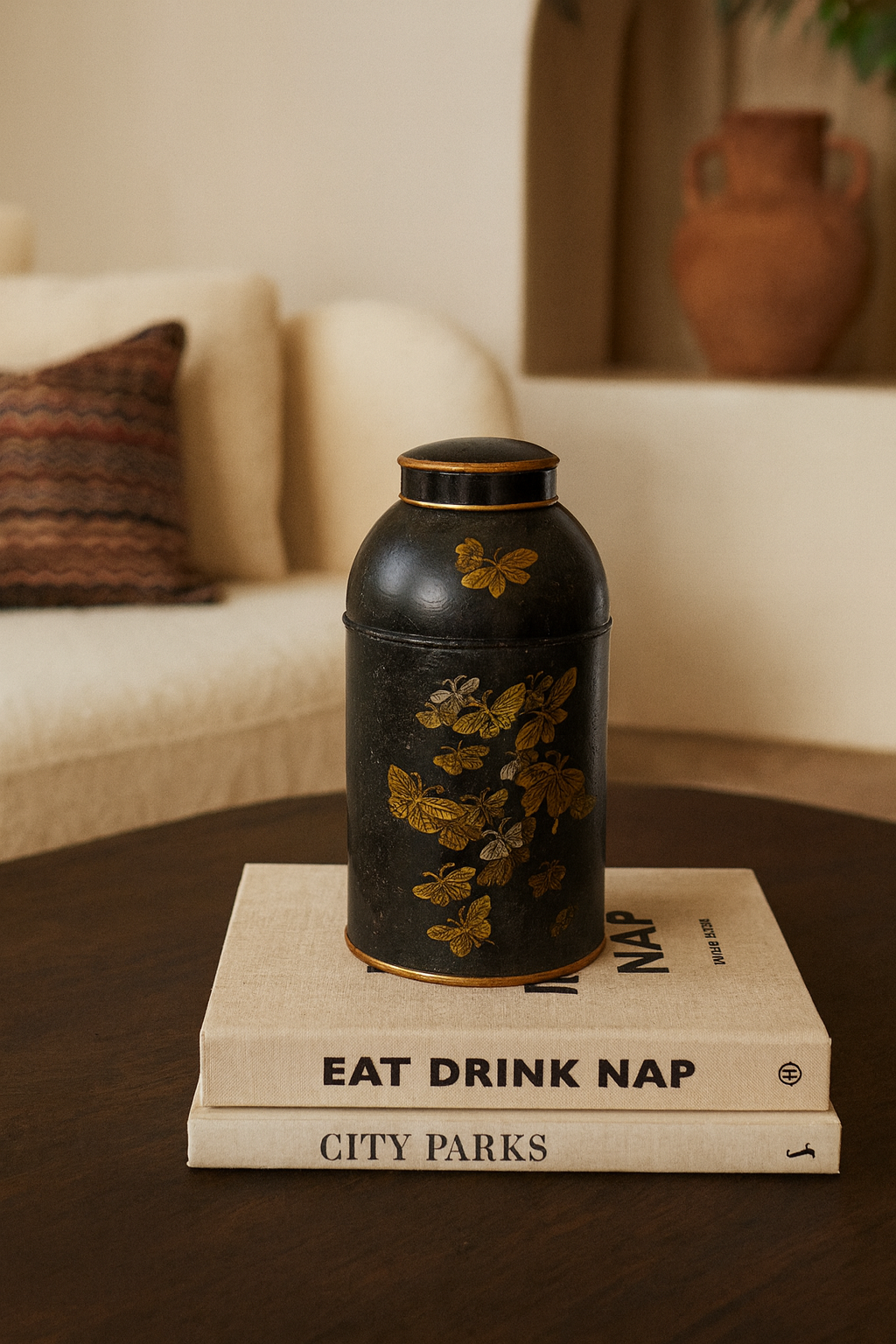 Decorative black vase with gold floral patterns on a stack of books in a cozy living room.